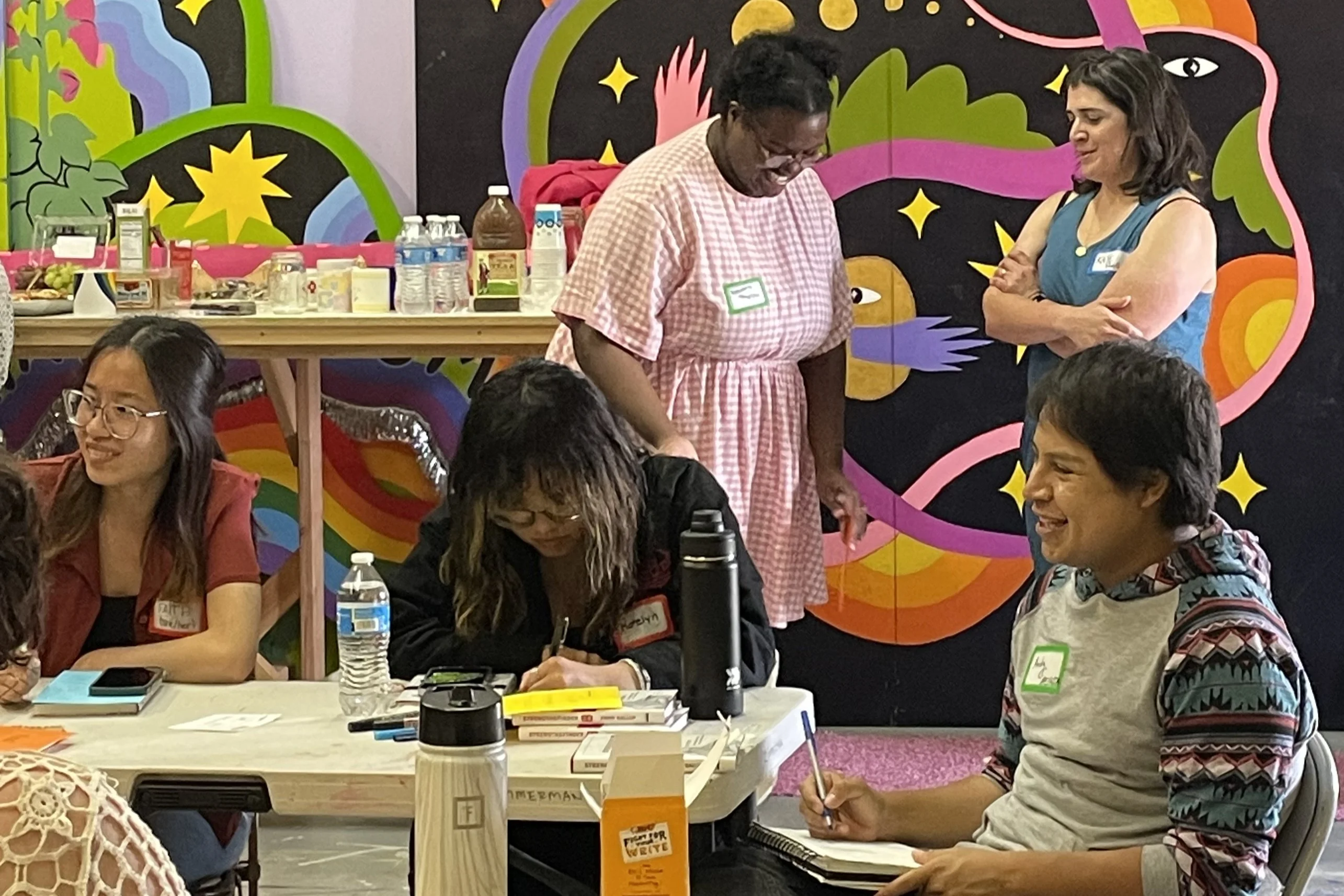 People in a workshop with a colorful mural in the background.